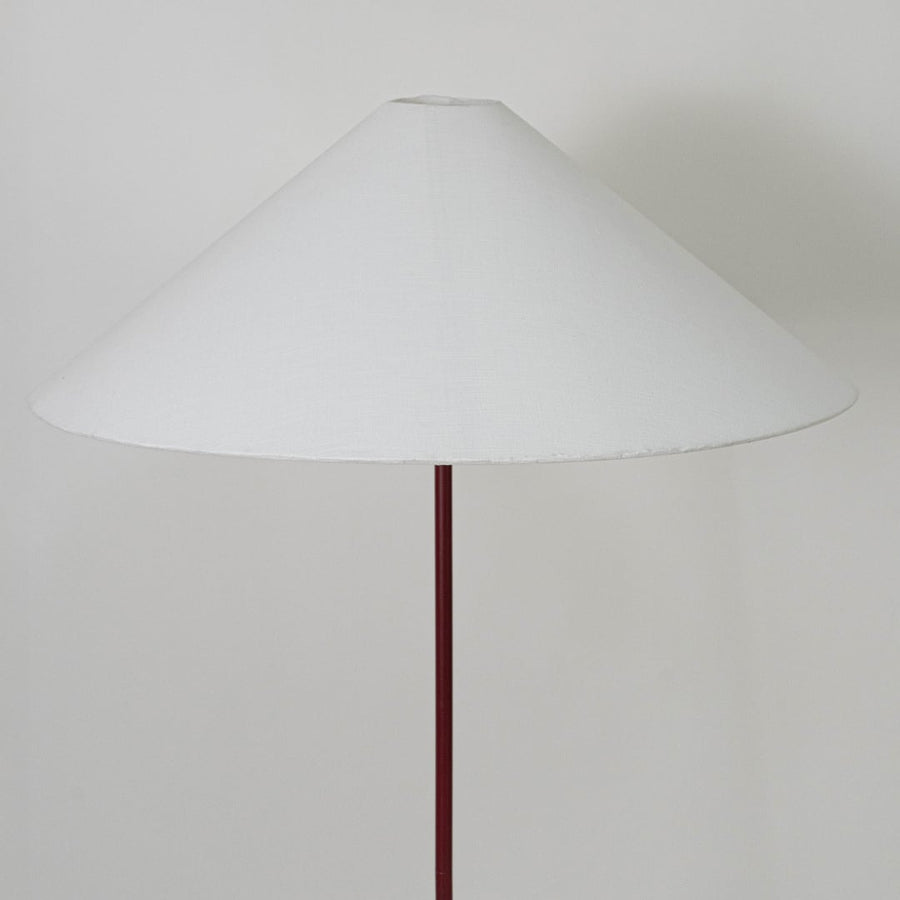 Large white conical lampshade supported by slim maroon rod designed to diffuse warm ambient light elegantly.