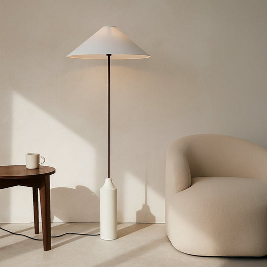 White and maroon floor lamp placed next to a beige chair and wooden table in cozy minimalist interior setting.