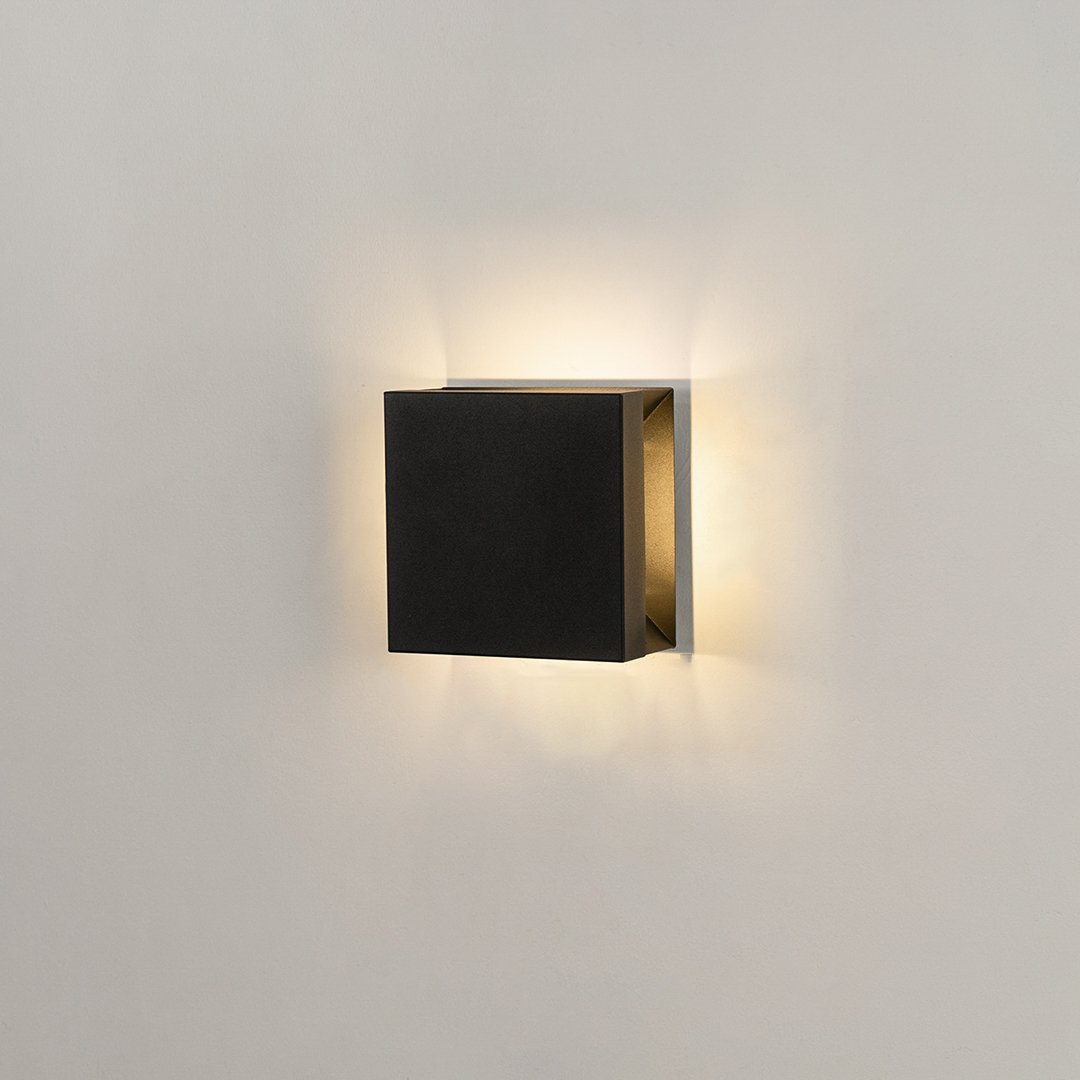 Modern square black aluminum outdoor wall sconce on white background casting warm multi-directional up and down light.