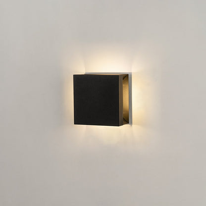 Modern square black aluminum outdoor wall sconce on white background casting warm multi-directional up and down light.