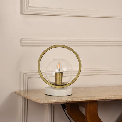 Golden ring table lamp unlit on white background featuring glass globe and marble base suited for modern minimal home decor.
