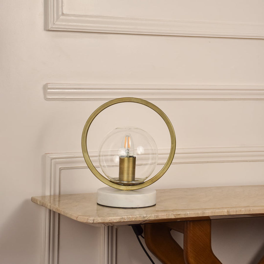 Golden ring table lamp unlit on white background featuring glass globe and marble base suited for modern minimal home decor.