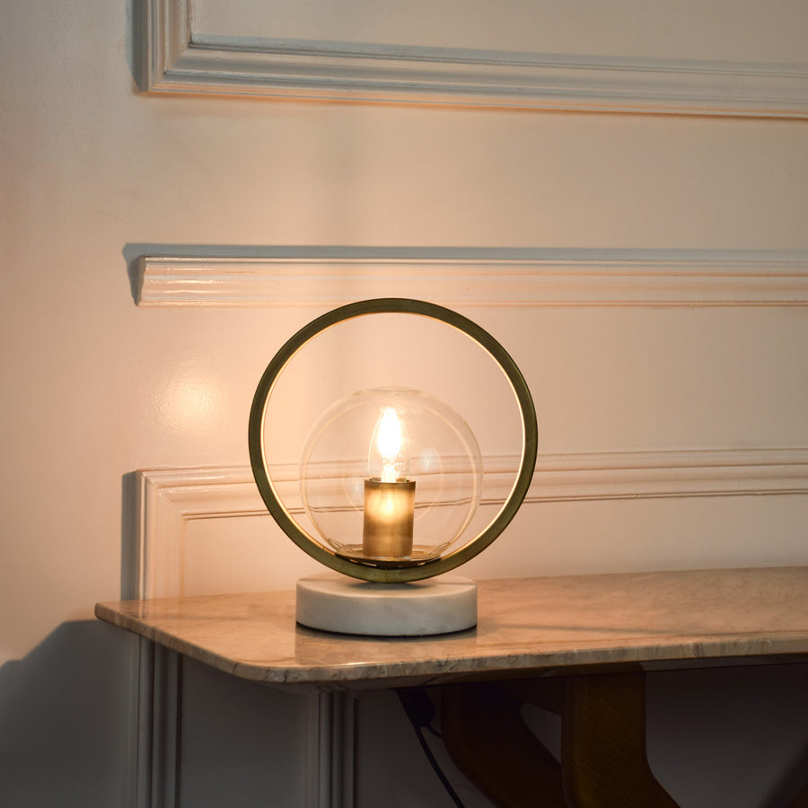 Circular metal table lamp with exposed bulb design creating warm ambient lighting for modern living spaces.