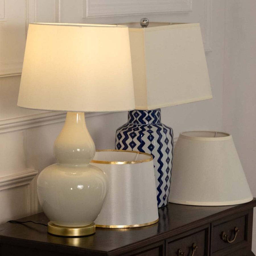 Cream shade white ceramic table lamp on wooden sideboard with light off beside decorative vases for modern cozy décor.