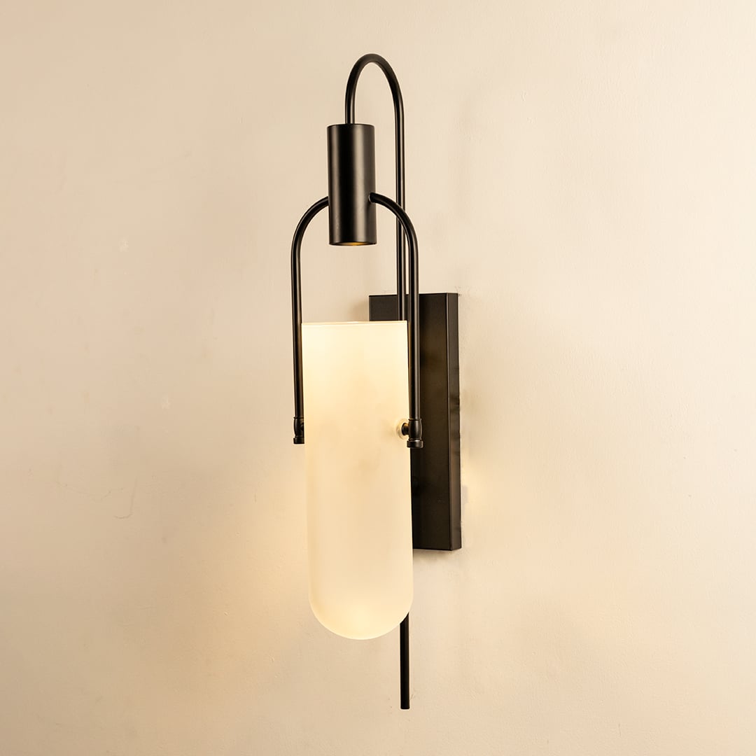 Black metal wall sconce with frosted glass shade glowing softly on white background for ambient lighting.