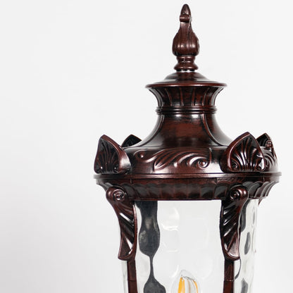 Closeup of brown pillar lamp with detailed carved frame and glass panels showing elegant outdoor gate and garden lighting.