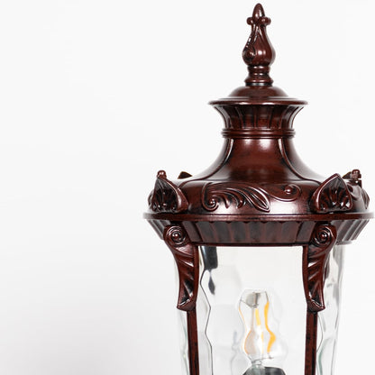Closeup of antique brown pillar light showing carved frame detailing and patterned clear glass for elegant outdoor lighting.