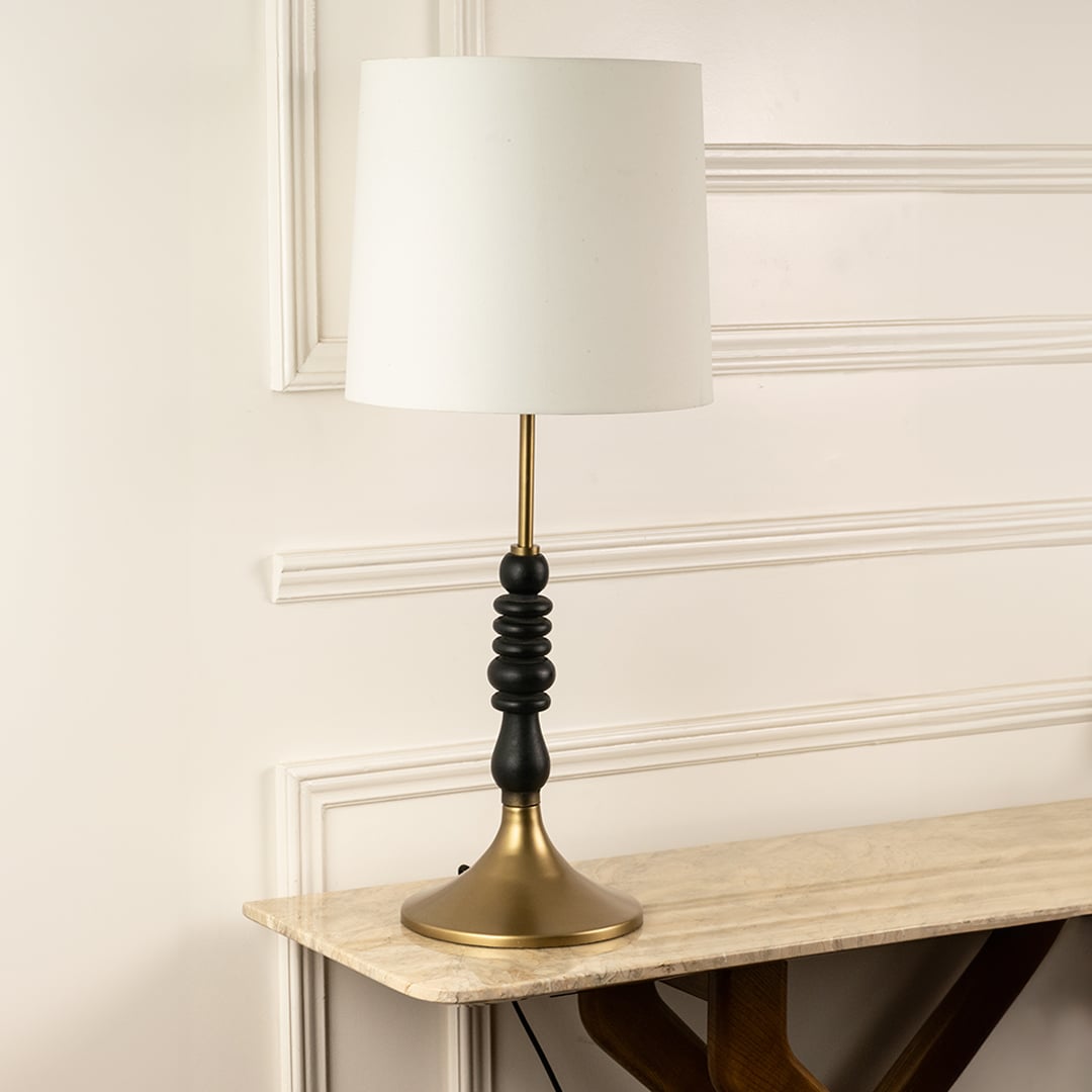 White fabric shade table lamp with black turned wood base and brass accents for elegant bedside and console decor.