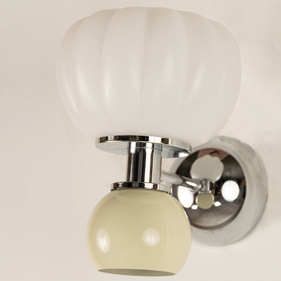 Macro view of polished chrome metal finish and texture of ribbed frosted white glass and glossy beige glass on modern wall light fixture.