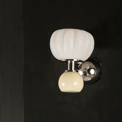 Unlit modern wall sconce displaying pumpkin shape white glass and round beige glass shades with chrome metal body on plain white background.