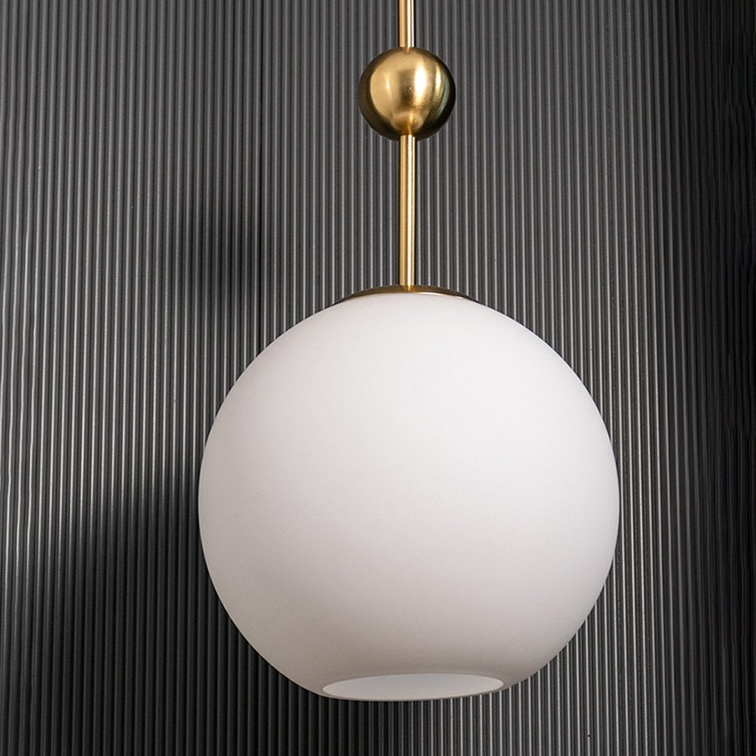 A gold and white glass pendant light with lights off on a dark vertical panel background emphasizing its frosted spherical shade and metallic gold accents.