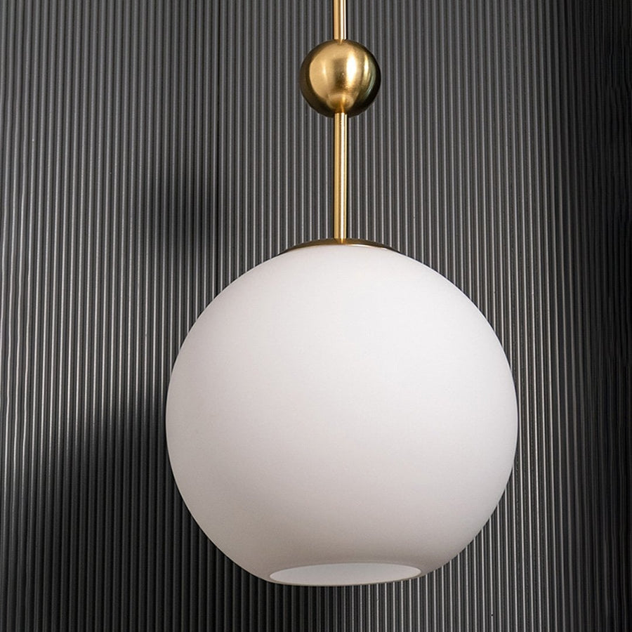 A gold and white glass pendant light with lights off on a dark vertical panel background emphasizing its frosted spherical shade and metallic gold accents.