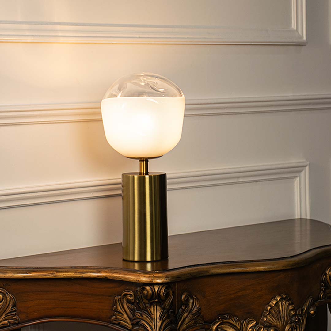White glass table lamp with brass metal base and illuminated globe shade creating sophisticated modern ambient lighting.