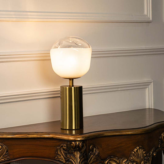 White glass table lamp with brass metal base and illuminated globe shade creating sophisticated modern ambient lighting.