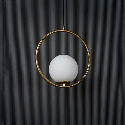 A circular pendant lamp displayed with the light off against a deep black background showing the clean round form and gold ring with subtle reflections.