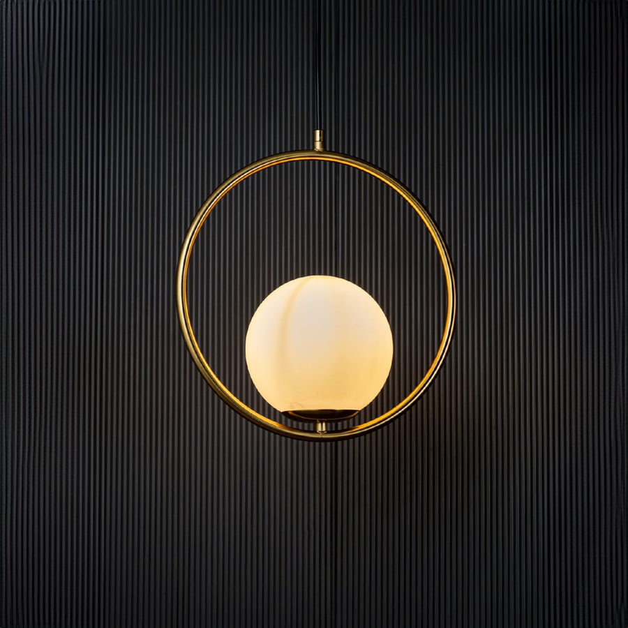 A circular pendant lamp illuminated against a dark black background creating a warm ambient glow that highlights the golden ring and smooth white globe.