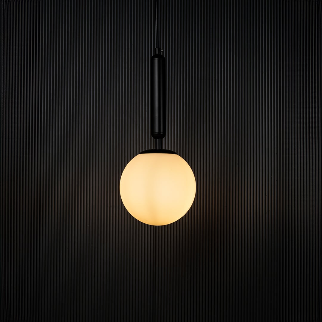 A glowing pendant light with the bulb on set against a dark black backdrop emphasizing its warm illumination and contemporary spherical form.
