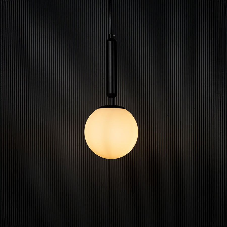 A glowing pendant light with the bulb on set against a dark black backdrop emphasizing its warm illumination and contemporary spherical form.