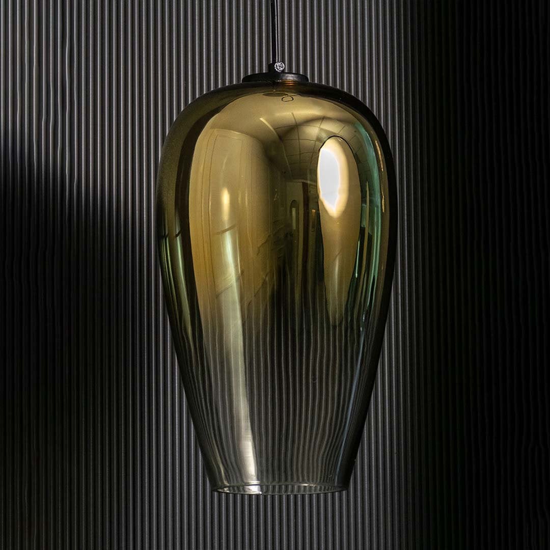 An amber tinted glass pendant light shown with lights off against a dark background emphasizing its tall sculpted silhouette and glossy finish.