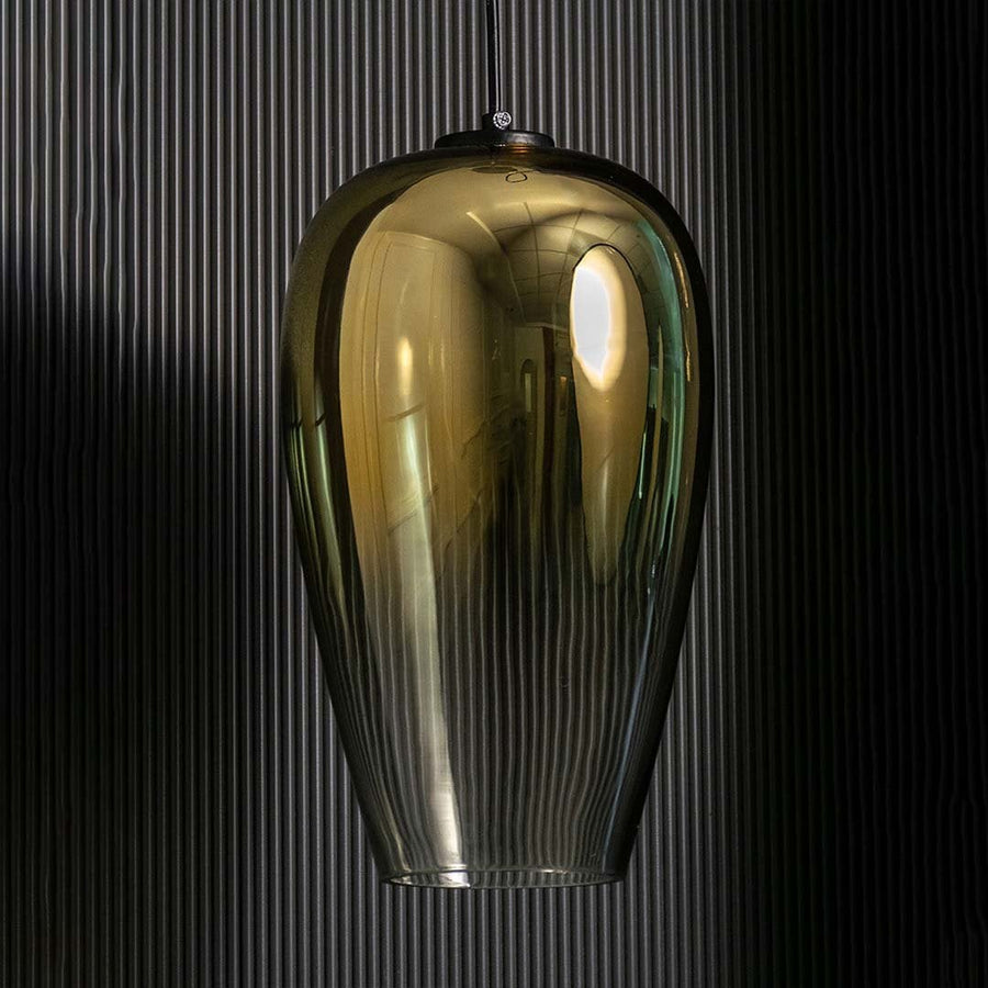 An amber tinted glass pendant light shown with lights off against a dark background emphasizing its tall sculpted silhouette and glossy finish.