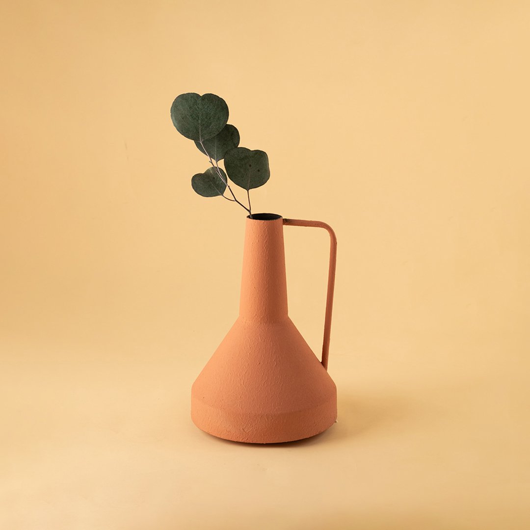 Matte orange metal vase with handle and leaf stem for modern minimalist home decor and vibrant table styling.