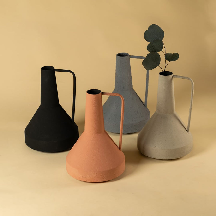 Modern ceramic pitcher collection in gray black terracotta and cream with metal handles featuring eucalyptus stems on neutral warm background aesthetic.