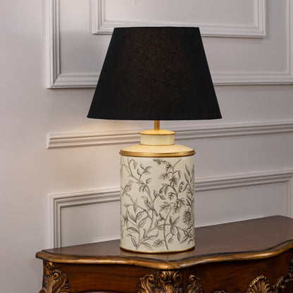 Table lamp featuring a patterned ceramic base with leaf detailing and a black fabric lampshade displayed on a white background.