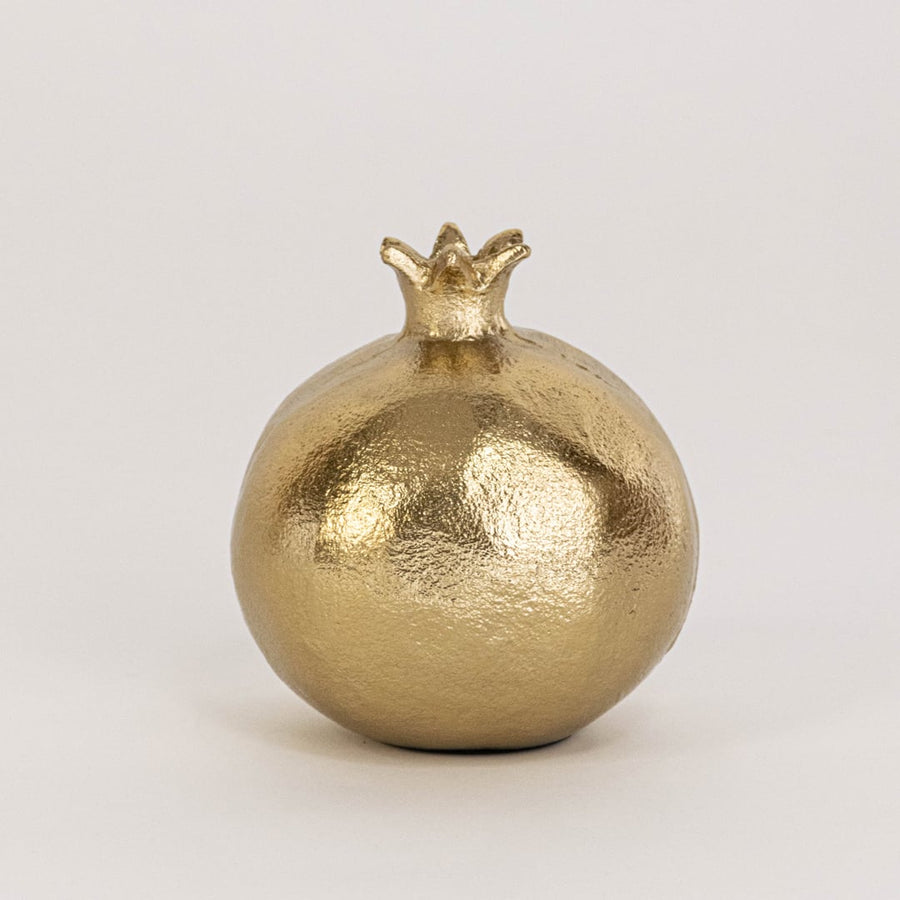 Gold pomegranate accent piece on a plain white backdrop highlighting its handcrafted surface and detailed seed pattern