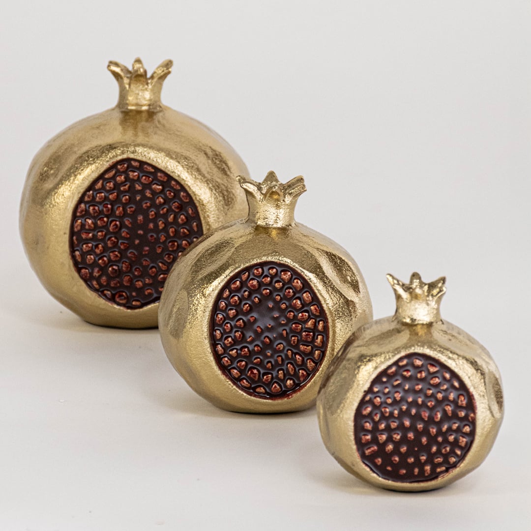 Gold pomegranate decorative piece shown as part of a grouped display highlighting its artistic seed detailing and sculpted form