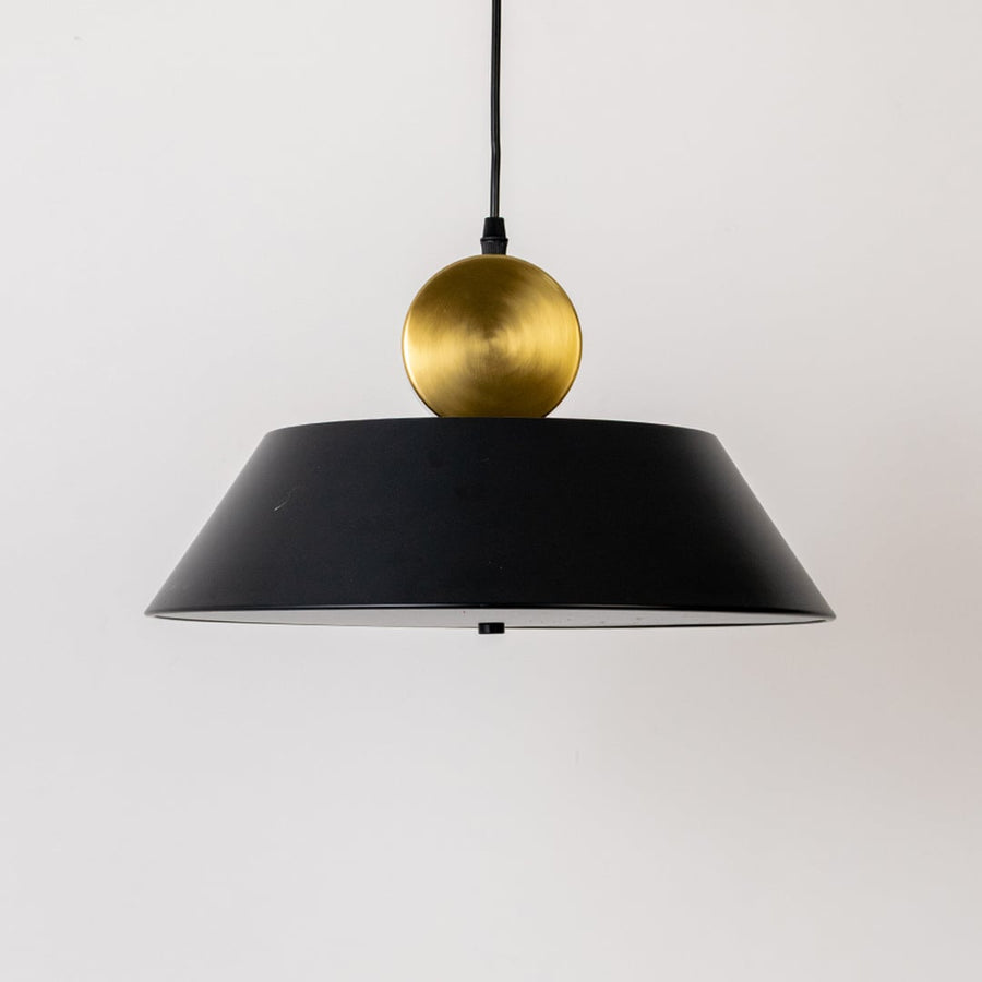 Closeup of black metal pendant light with gold sphere detail highlighting smooth finish premium materials and modern lighting design.