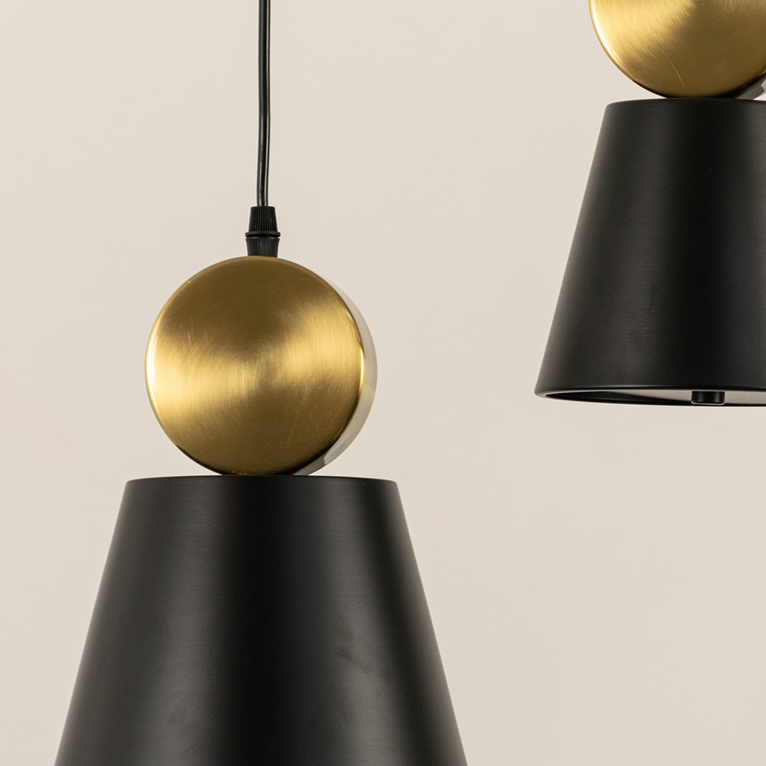 Close up of modern pendant lights with black cone shades and round gold tops hanging from black cords against a light background.