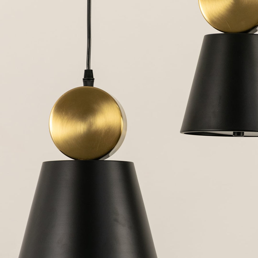 Close up of modern pendant lights with black cone shades and round gold tops hanging from black cords against a light background.