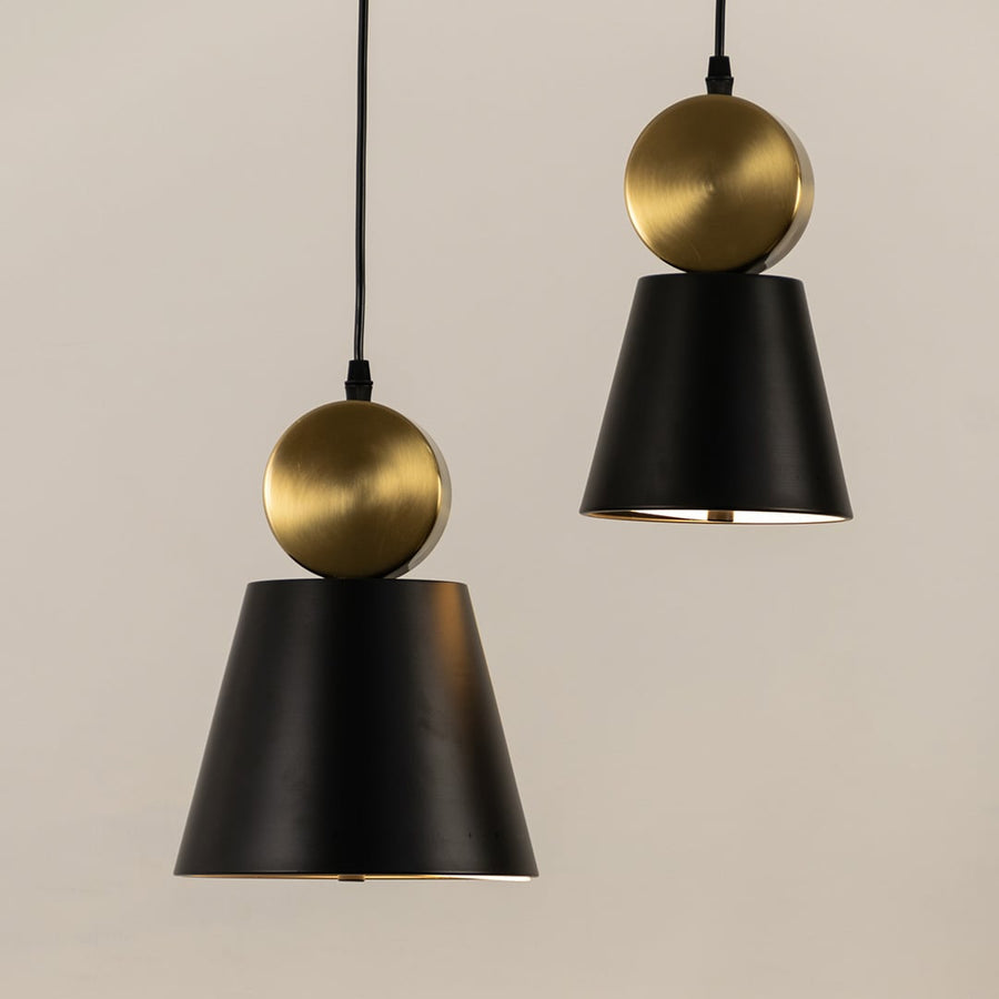 Two modern pendant lights with black cone shades and round gold tops hanging from black cords against a light background.