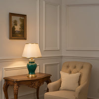 Elegant green table lamp with golden base and white shade styled on wooden side table in living room.