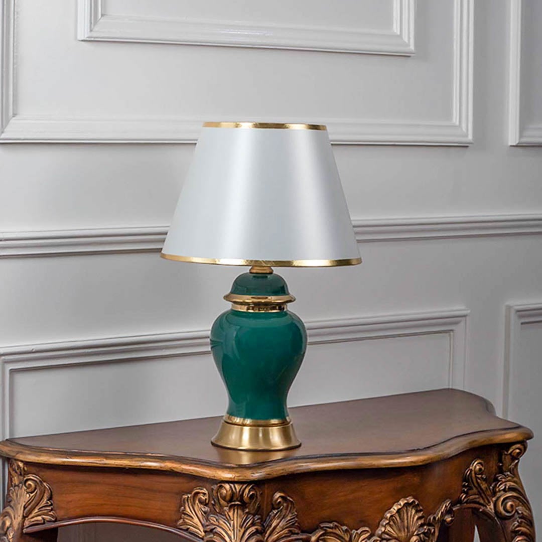 Green and gold table lamp with white lampshade turned off against white background.