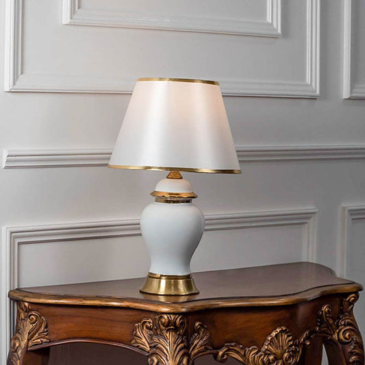 Table lamp with white ceramic base and white fabric shade on wooden table minimal classic lighting for bedroom decor.