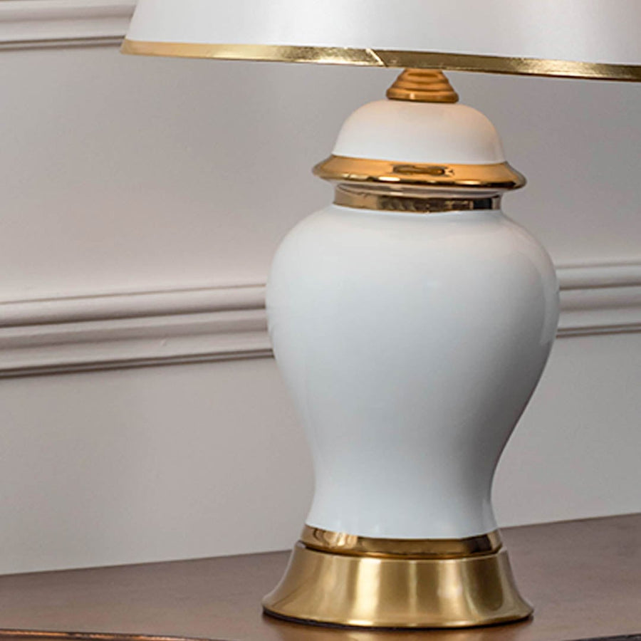 Closeup of white ceramic table lamp with glossy finish golden base and tapered lampshade for home decor.