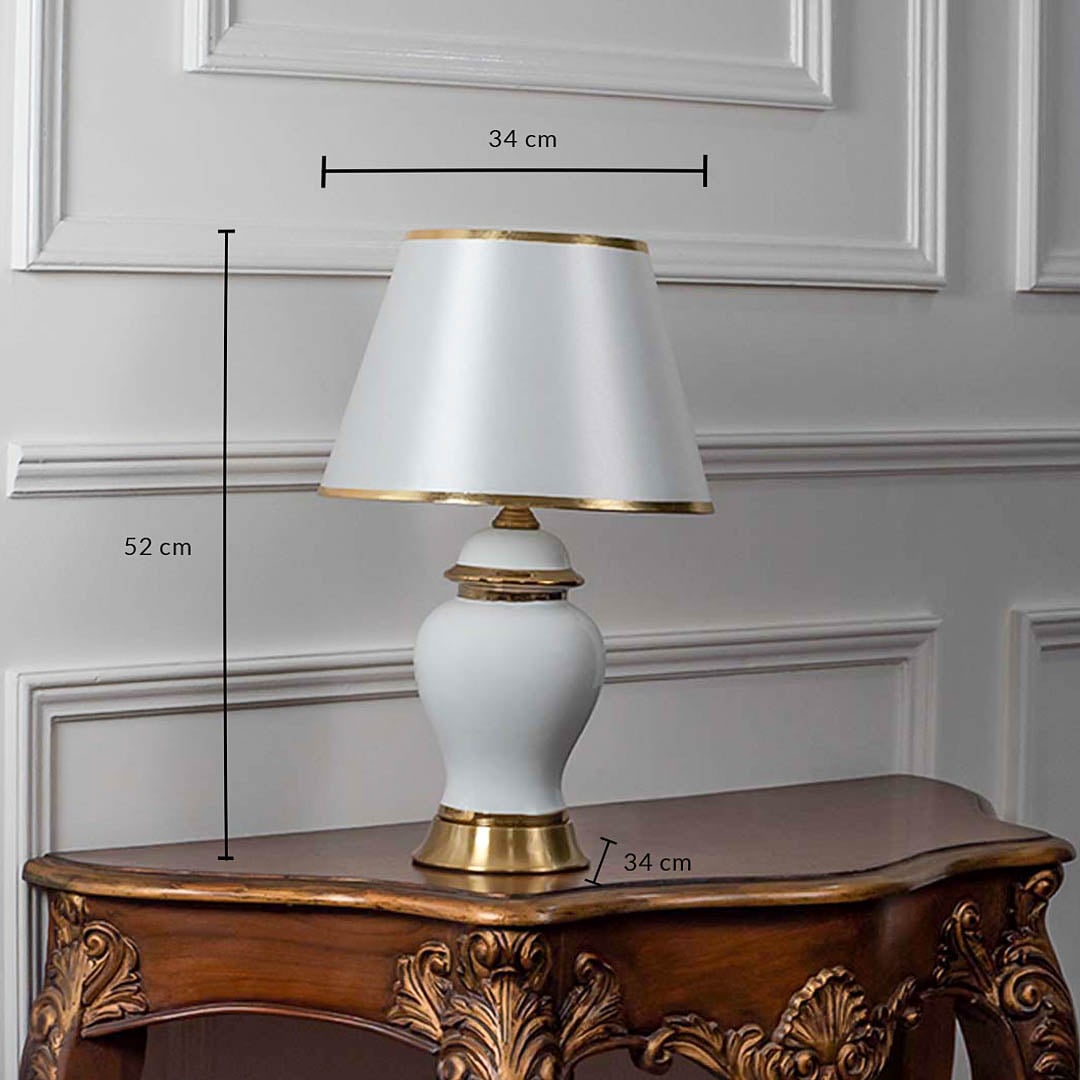 White ceramic table lamp with tapered shade and golden base shown with 52cm height and 34cm width.