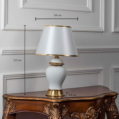 White ceramic table lamp with tapered shade and golden base shown with 52cm height and 34cm width.