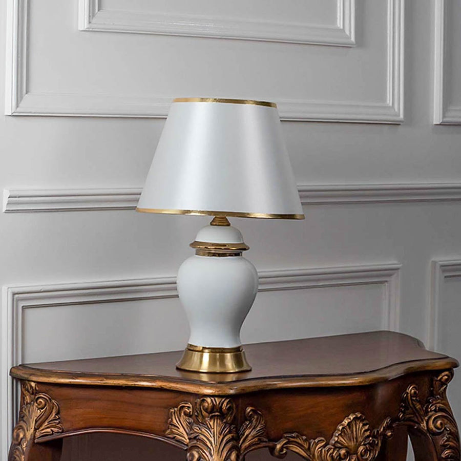 White ceramic table lamp turned off with tapered fabric shade and golden accents on plain white background.