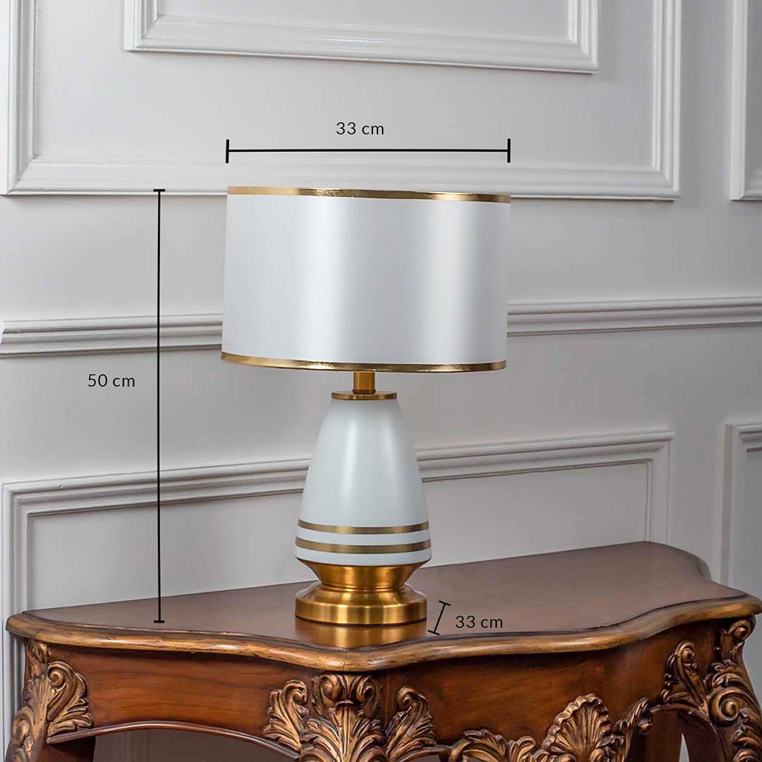 White ceramic table lamp with fabric drum shade and golden detailing shown with 50cm height and 33cm width.