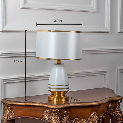 White ceramic table lamp with fabric drum shade and golden detailing shown with 50cm height and 33cm width.