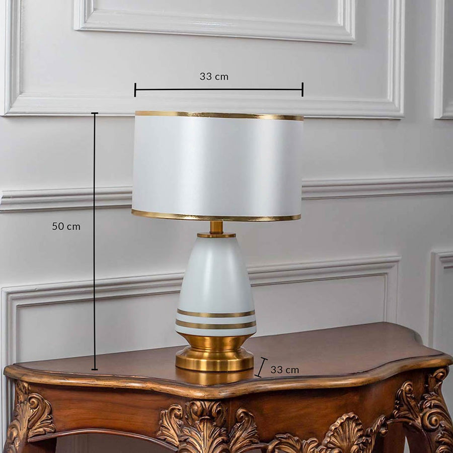 White ceramic table lamp with fabric drum shade and golden detailing shown with 50cm height and 33cm width.
