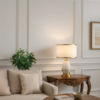 White ceramic table lamp with golden base and drum fabric shade adding elegant lighting to modern living room decor.