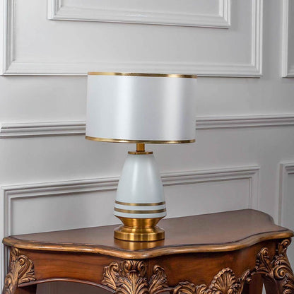 White ceramic table lamp turned off with drum shade and golden base displayed on plain white background decor.