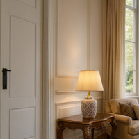 White and gold ceramic table lamp with printed base placed on wooden console in elegant living room interior decor.