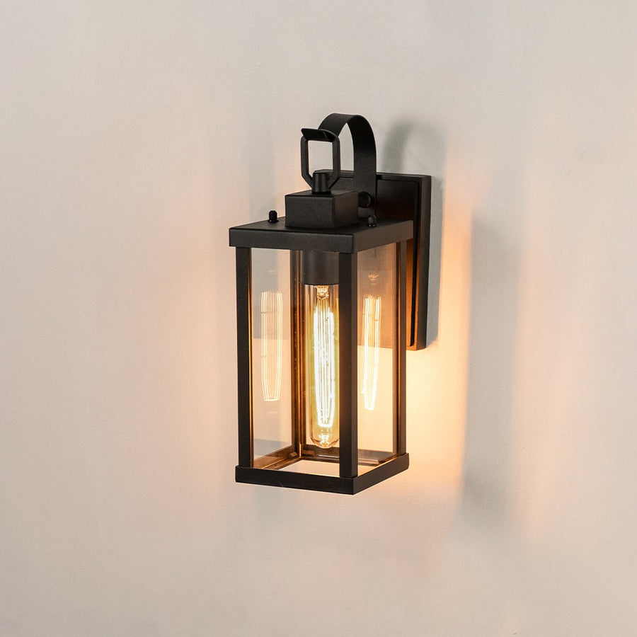 Modern black rectangular outdoor wall light on white background with clear glass panels illuminating a warm vintage glow.