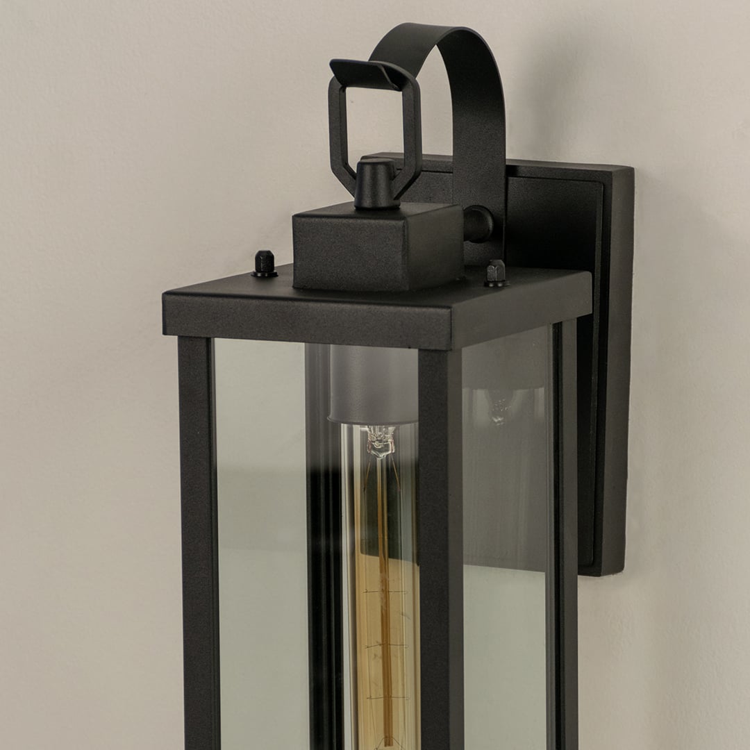 Closeup view of the antique brass finish and decorative scroll arm detail on the bottom of the classic glass wall lantern.