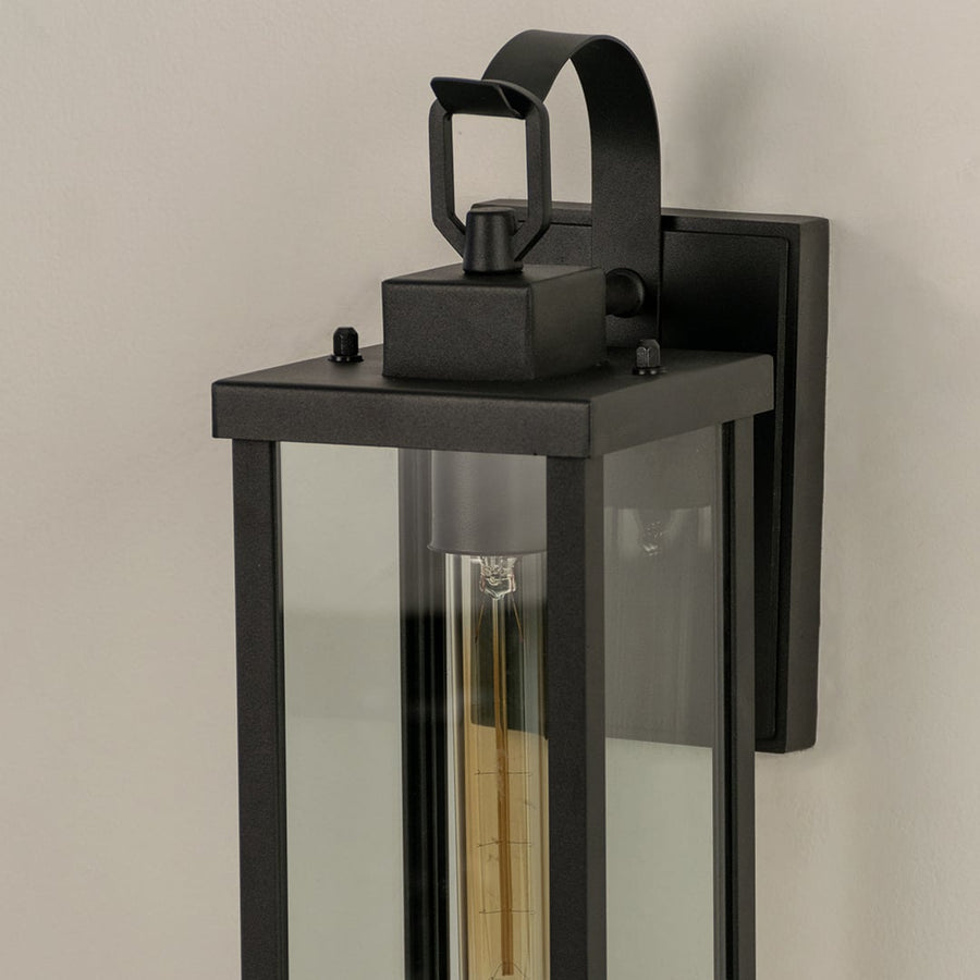 Closeup view of the antique brass finish and decorative scroll arm detail on the bottom of the classic glass wall lantern.