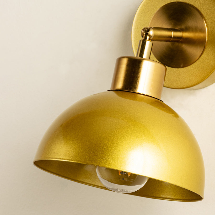Closeup of gold metal wall light with dome shade showcasing smooth finish and premium detailing for modern interior decor styling.